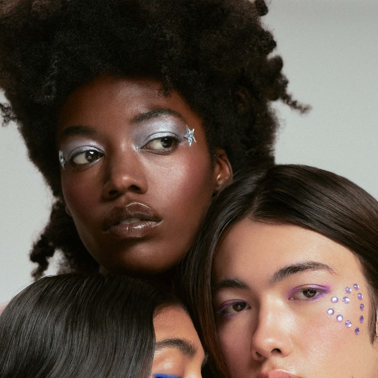 A close-up image of three people of colour wearing glittery makeup.